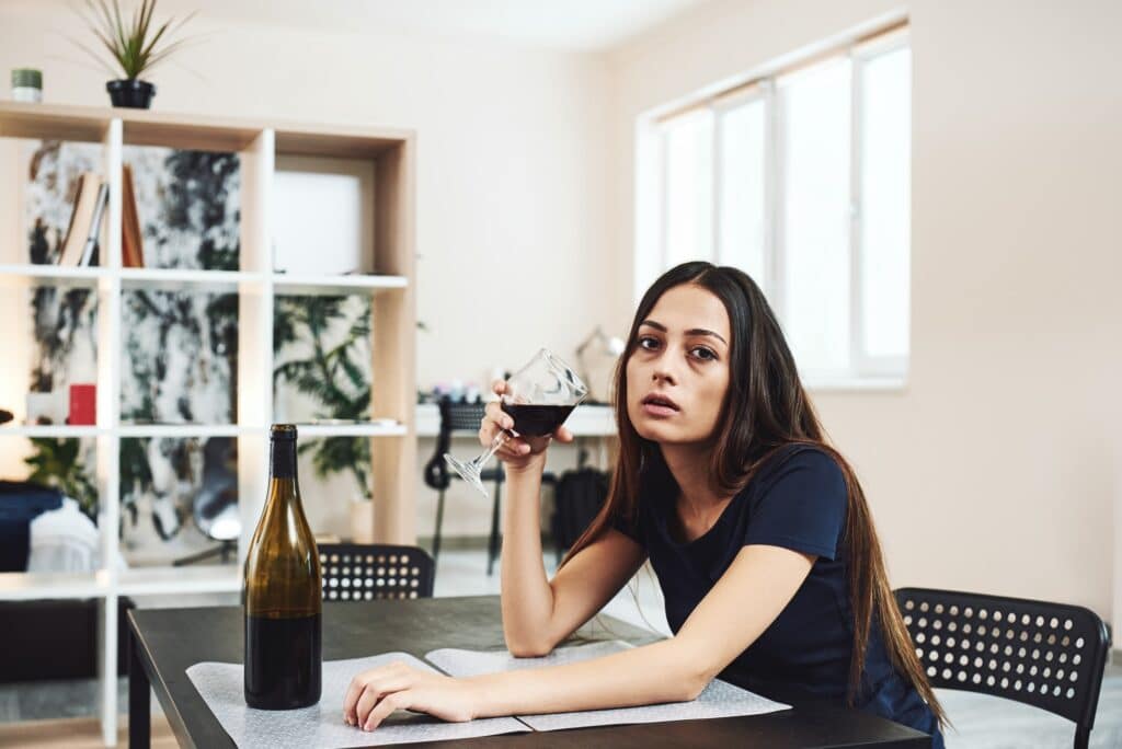 Alcoholism is a disease of the whole person. Young woman drinking red wine alone in kitchen at home