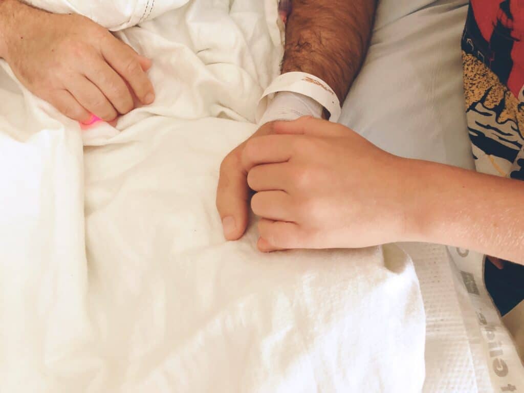 Child holding fathers hand in hospital.