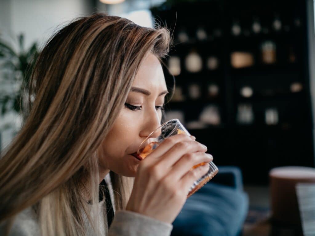 Young woman doing drinking alcohol cocktail glass holding up to mouth tasting restaurant bar