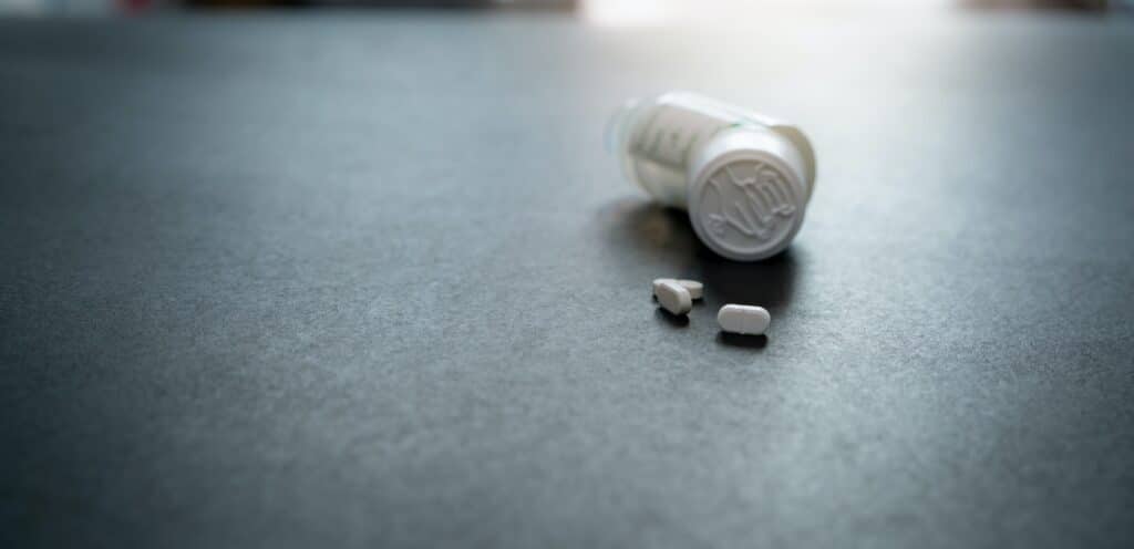 White tablets pills and blur child-resistant pill bottle on black table. Prescription drugs. Pharmac