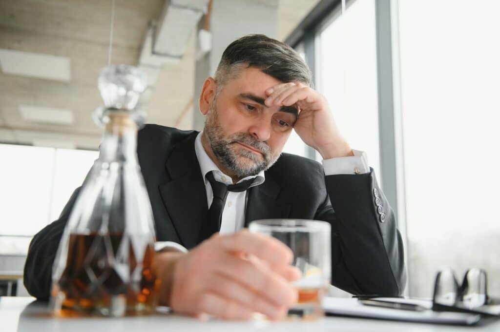 Old male employee drinking alcohol at workplace