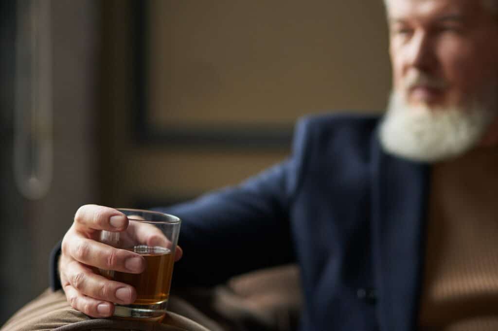 Successful middle aged business man holding glass of alcohol scotch whiskey in his hand while
